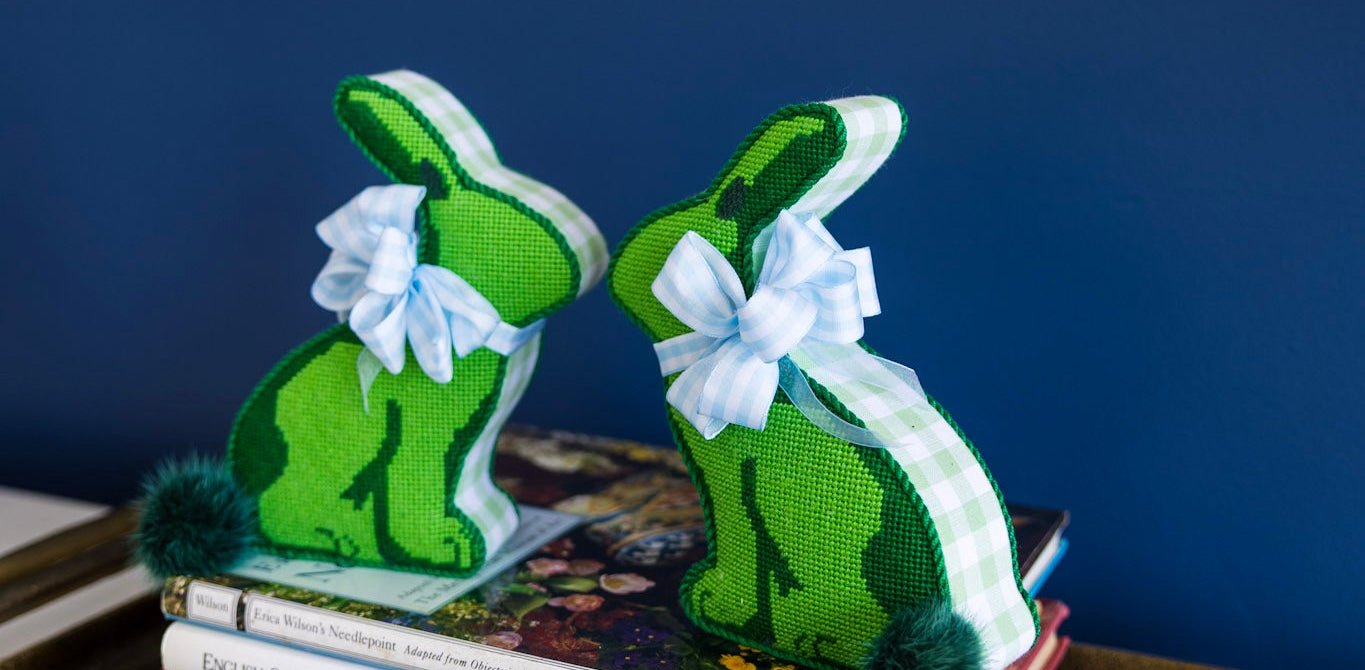 Green bunny bookends on a stack of books against a blue wall with a framed picture.