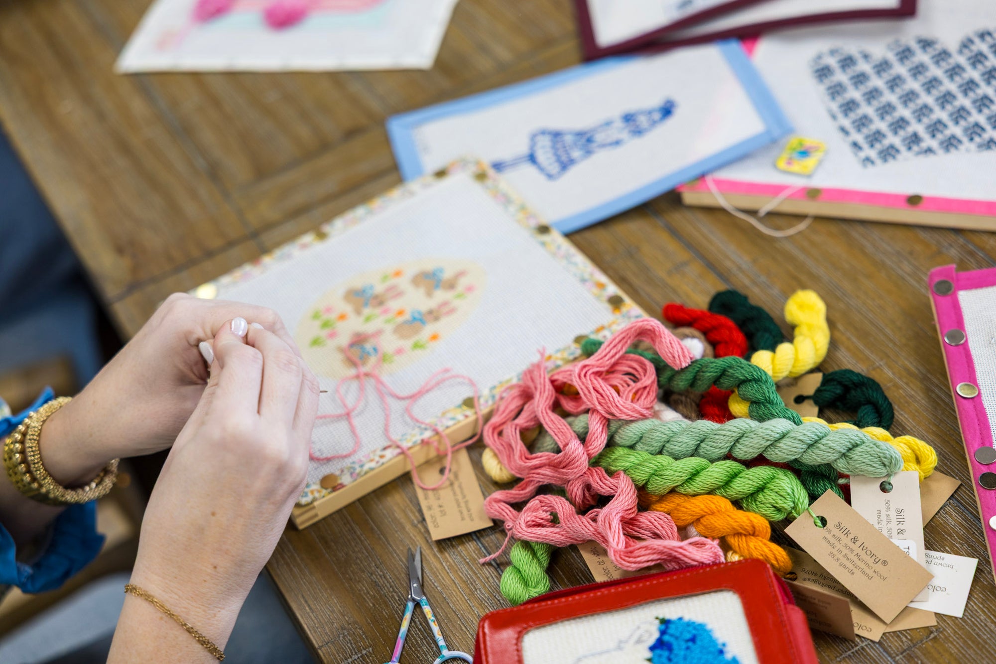 Person working on a cross-stitch project with colorful threads and patterns in the background.