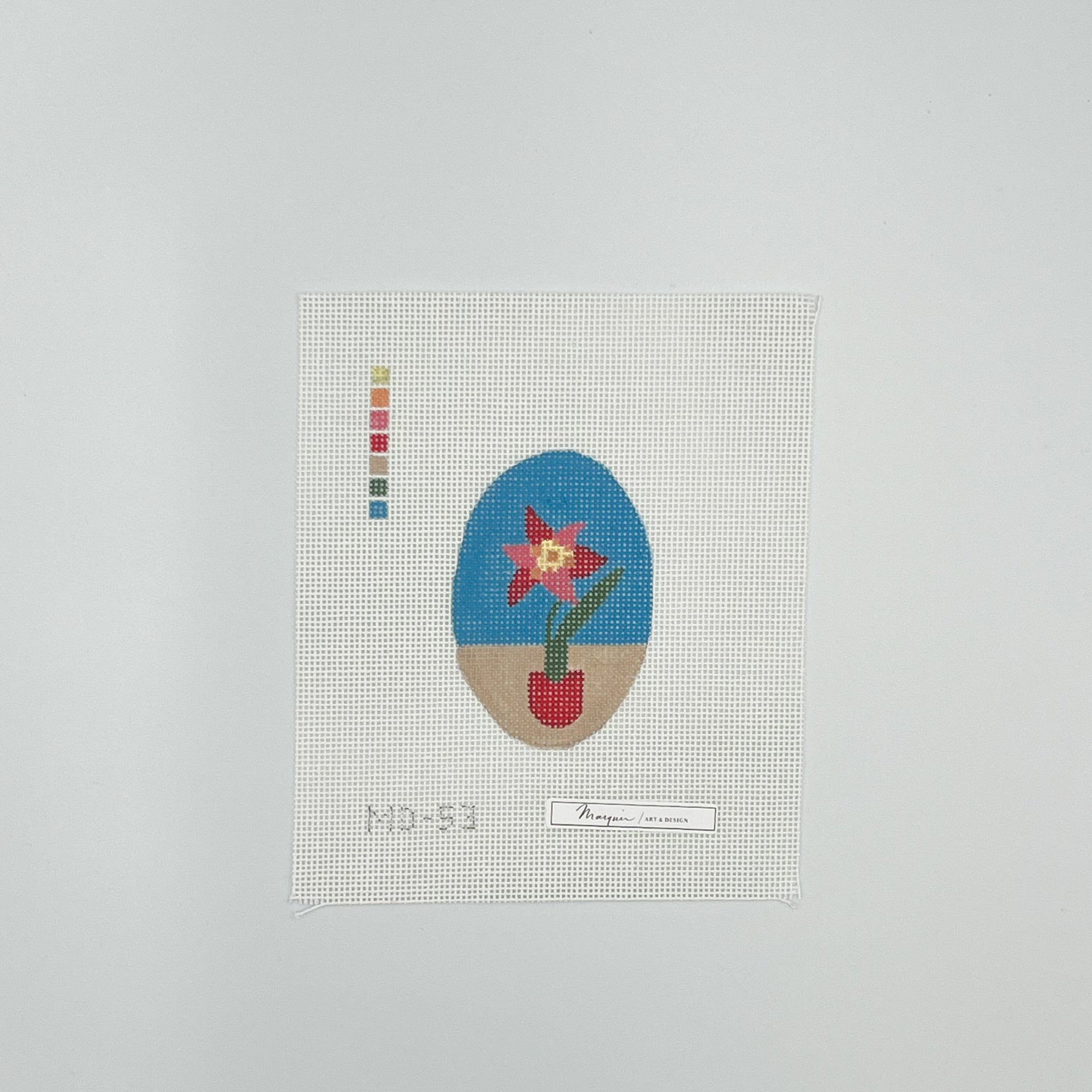 Needlepoint flower design on a white canvas with a blue and tan background