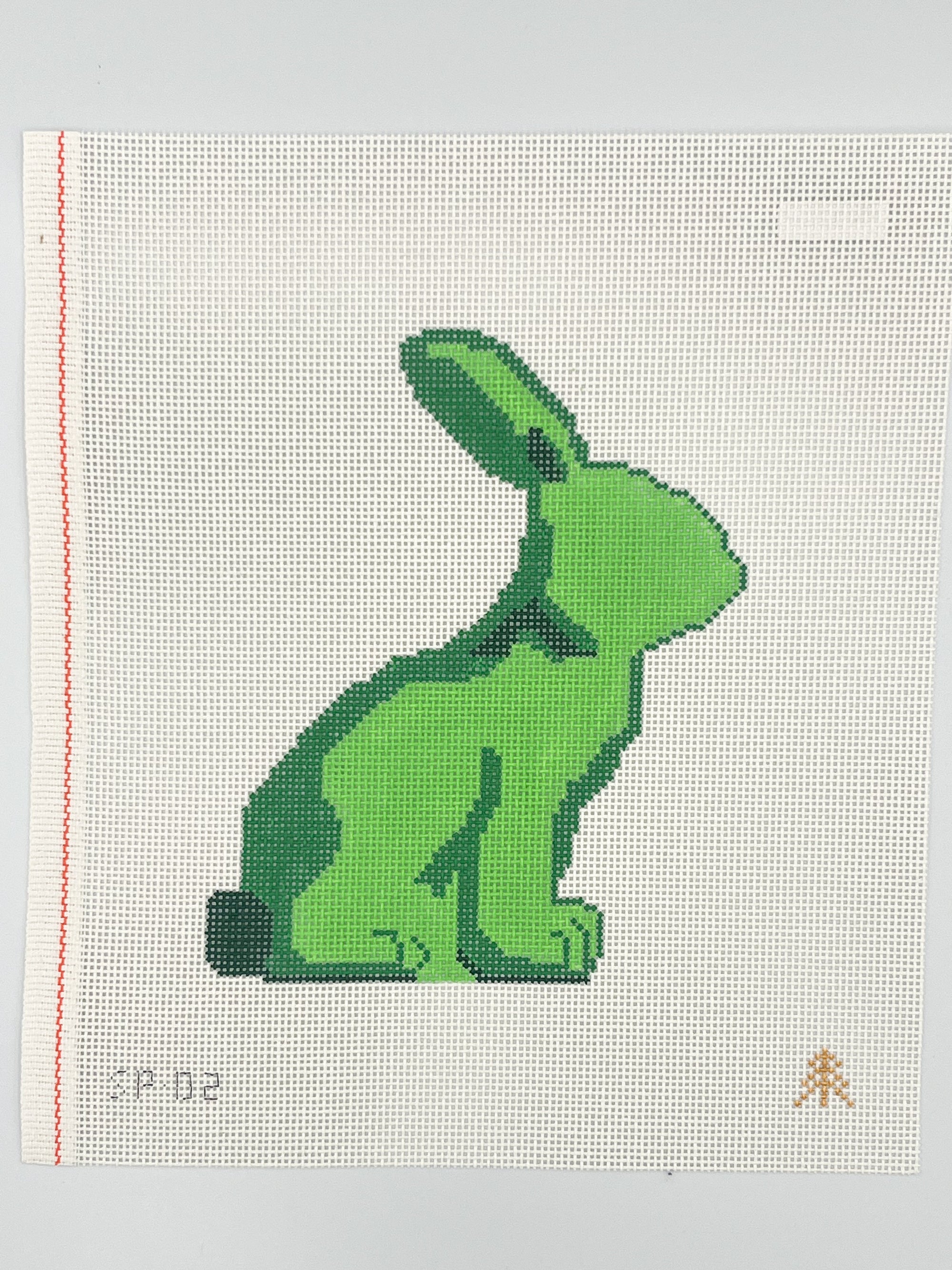 Green cross-stitched bunny on a white fabric background